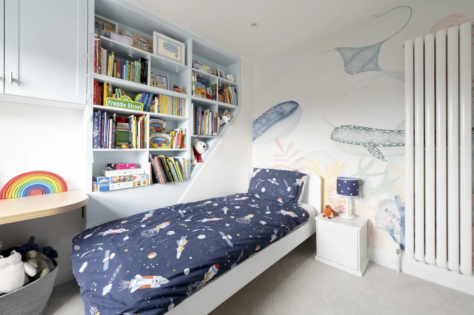 A boy's room in blue, with reading shelves within reach of the bed.